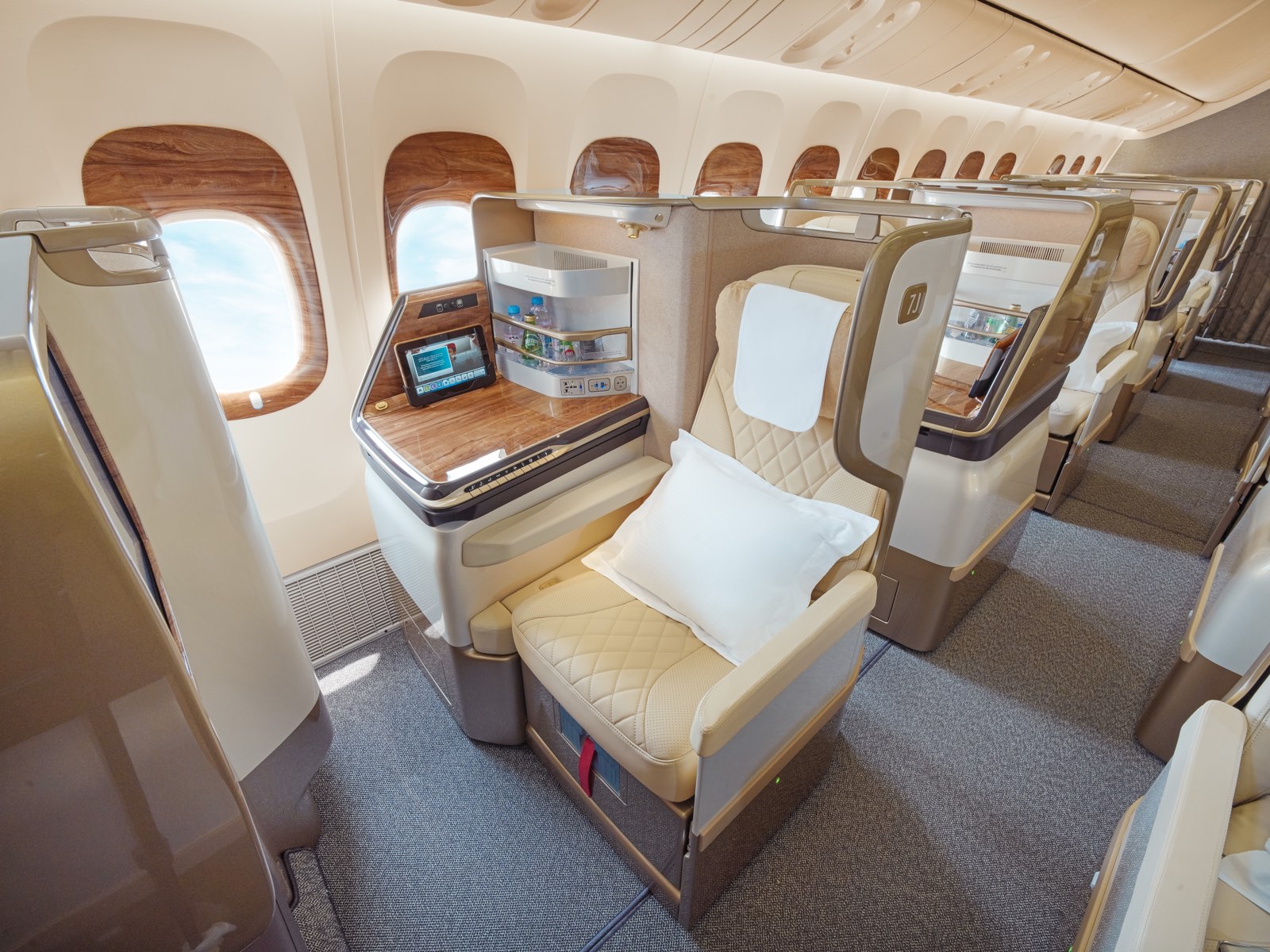 Eine umgebaute Business-Kabine der Emirates-Boeing-777 in 1-2-1, Sitz in champagnerfarbenem Leder mit Konsole in Holzoptik und den Suiten dahinter
