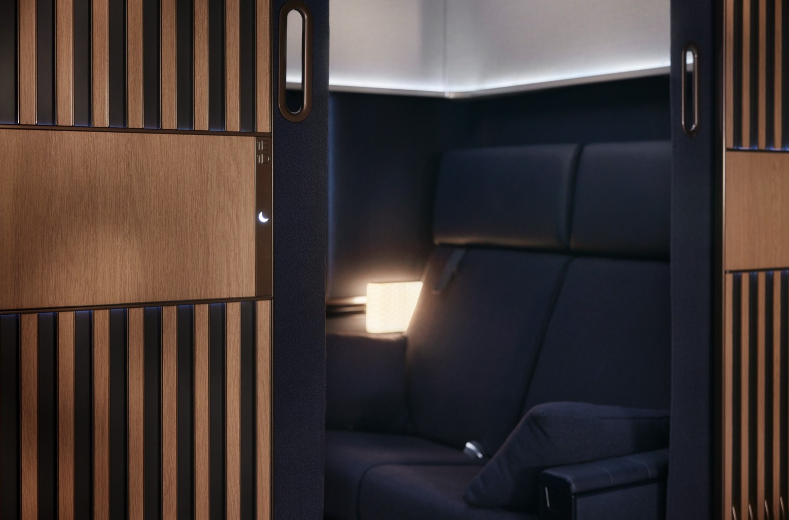 A Lufthansa Allegris first class suite seen from the aisle, its full-height door and wood-slat screen closed and a lamp lit inside