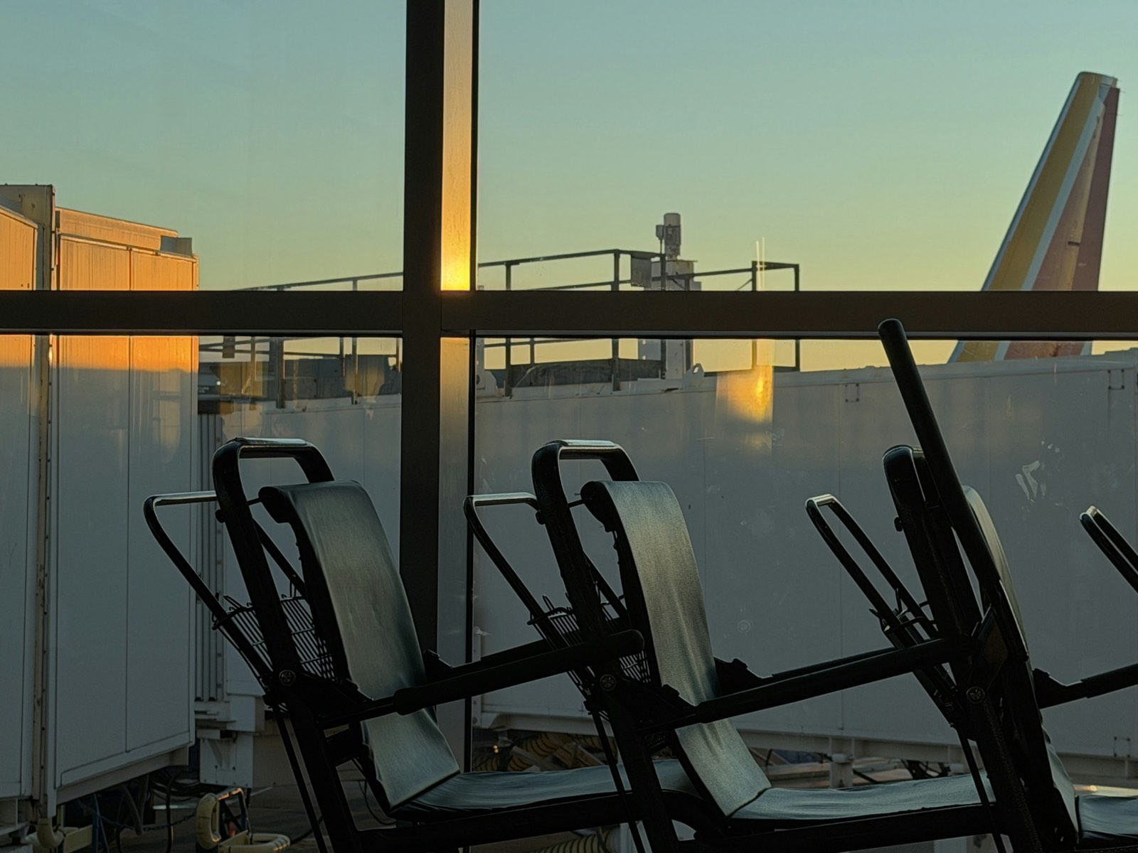 The tail of an aircraft seen from an airport terminal window at dusk