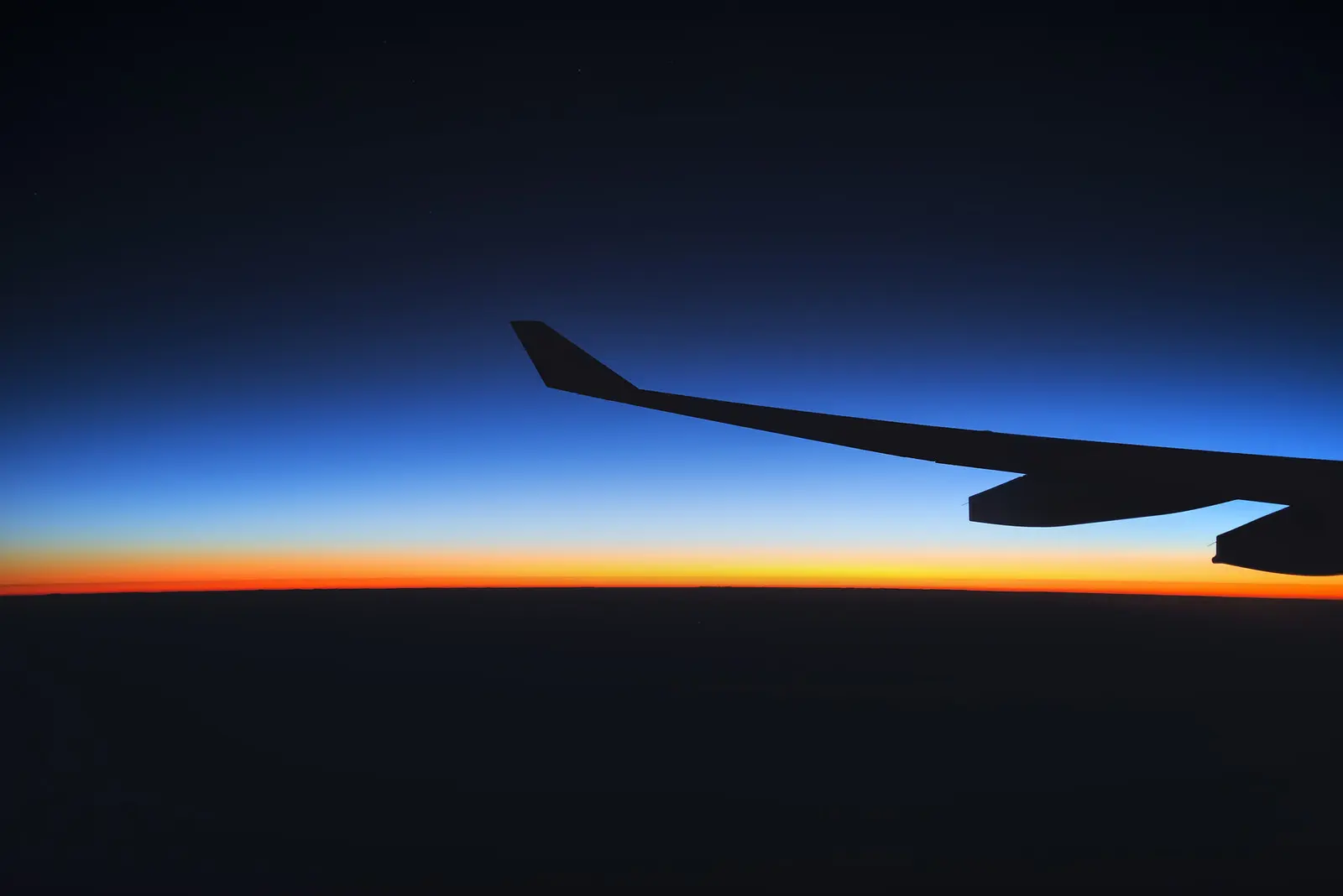An aircraft wing in silhouette against the first light of dawn.